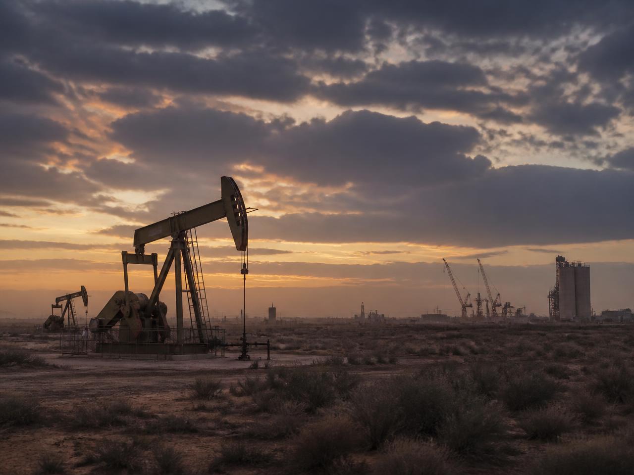 West Texas oil field pump jacks at dusk with construction cranes and silos on the horizon