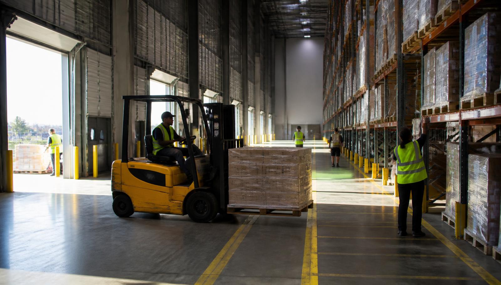 Forklift operator moving a pallet inside a distribution warehouse
